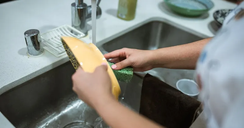 Person cleaning a yellow bowl using a sponge