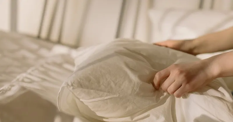 Person holding white textile pillowcase on a bed